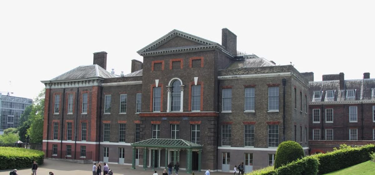The south front of Kensington Palace, its pedimented centre rising over the glazed visitor entrance with clipped yew cones on the lawn in front